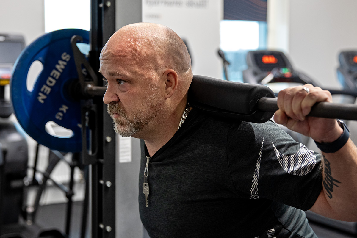 Skallig man med vit t-shirt lyfter tyngder på ett gym.